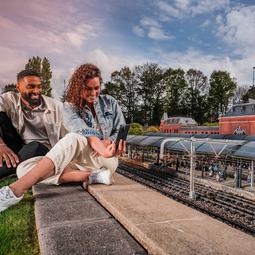 Stel zit naast een miniatuurspoorbaan en bekijkt de rijdende modeltreinen