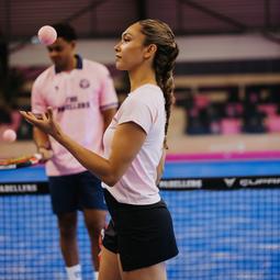 Vrouw gooit een bal omhoog op de padelbaan