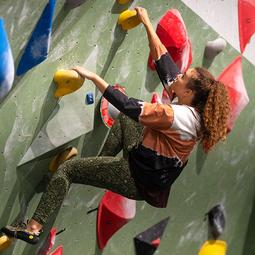 Deelnemer klimt aan een indoor boulderwand met gekleurde grepen.