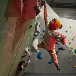 Kind klimt gezekerd omhoog langs een indoor klimwand tijdens een boulderles.