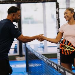 Twee personen geven elkaar een hand op de padelbaan